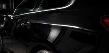Close-up of a glossy black car body panel with a chrome door handle and trim, photographed in a dark setting.